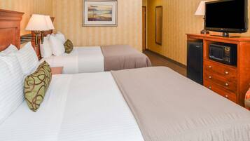A hotel room with two beds, a television, a microwave, and a painting on the wall.