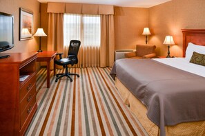 A hotel room with a bed, a desk, a chair, a television, and two lamps.