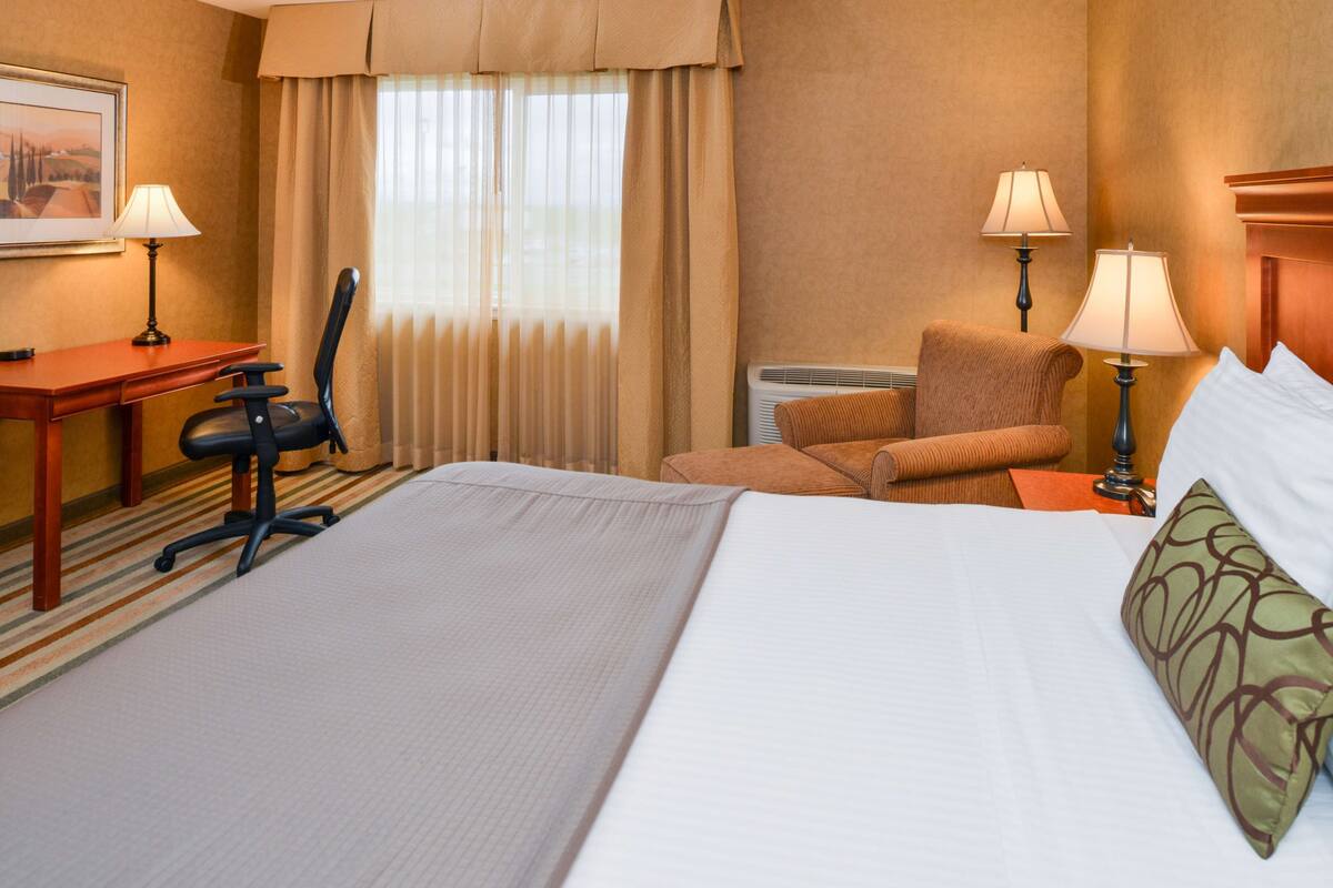A hotel room with a large bed, two chairs, a desk, and two lamps.