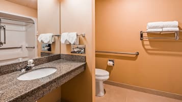 A bathroom with a granite countertop sink, a white toilet, and a towel rack with folded towels.