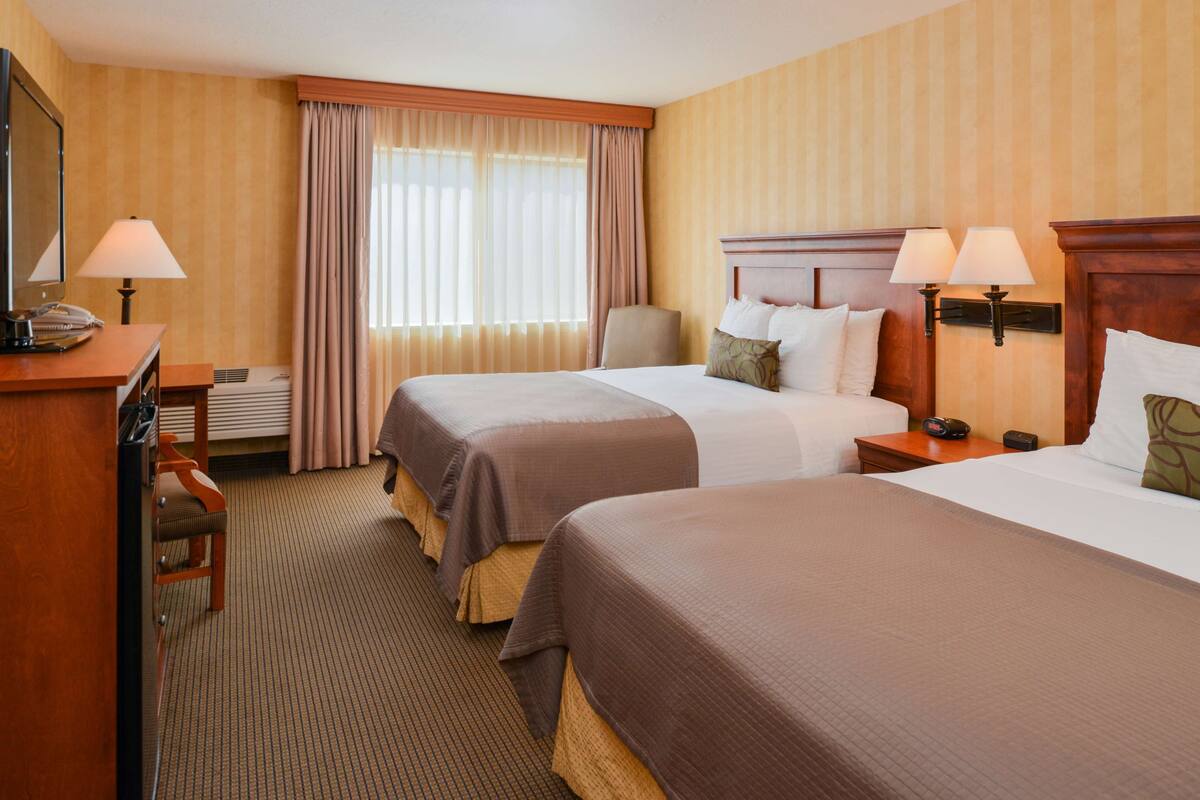 A hotel room with two beds, a desk with a telephone, a chair, and a window with curtains.