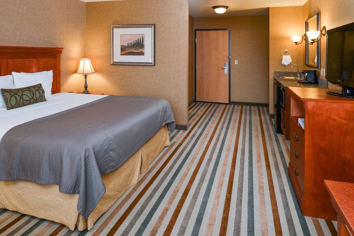 A hotel room with a large bed, a desk with a television, a bathroom with a shower, and a door leading to another room.