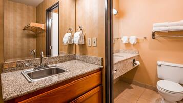 A bathroom with a granite countertop sink, wooden cabinets, a toilet, and a towel rack.
