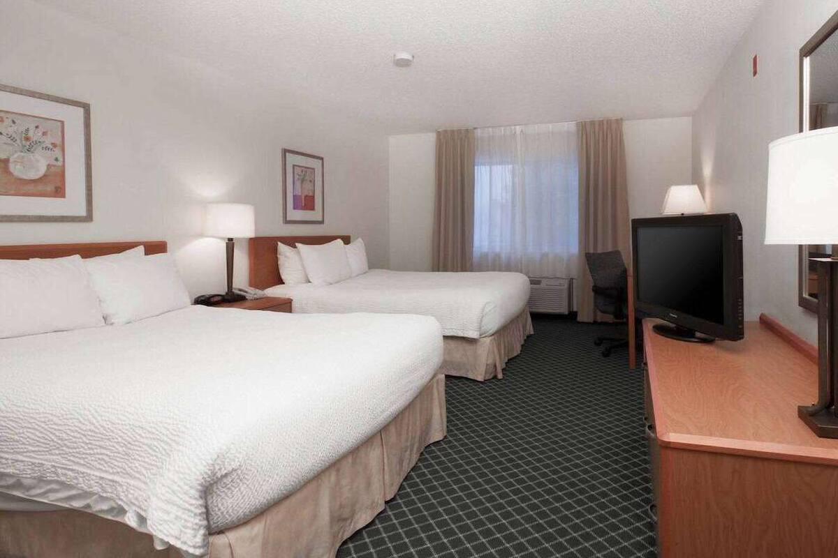 Une chambre d’hôtel avec deux lits, un bureau avec une télévision et une fenêtre avec des rideaux.