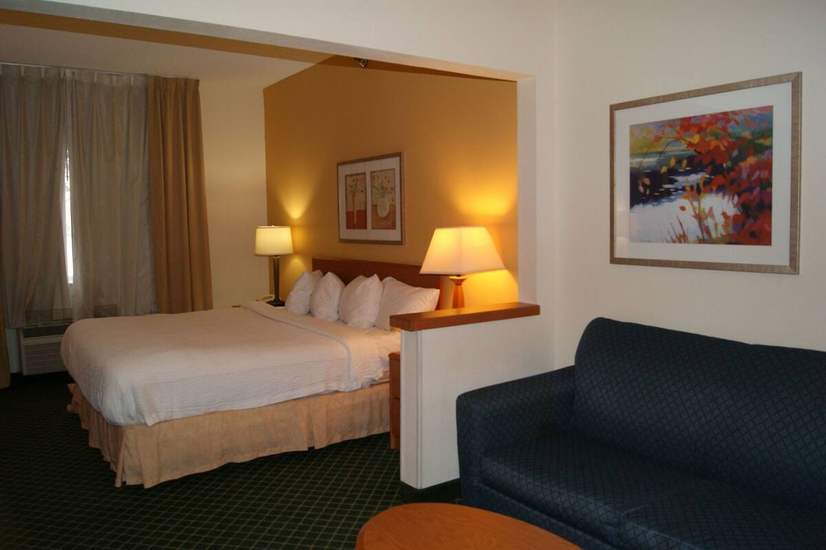 Une chambre d’hôtel avec un lit, deux lampes de chevet, un canapé, un tableau et une fenêtre avec des rideaux.