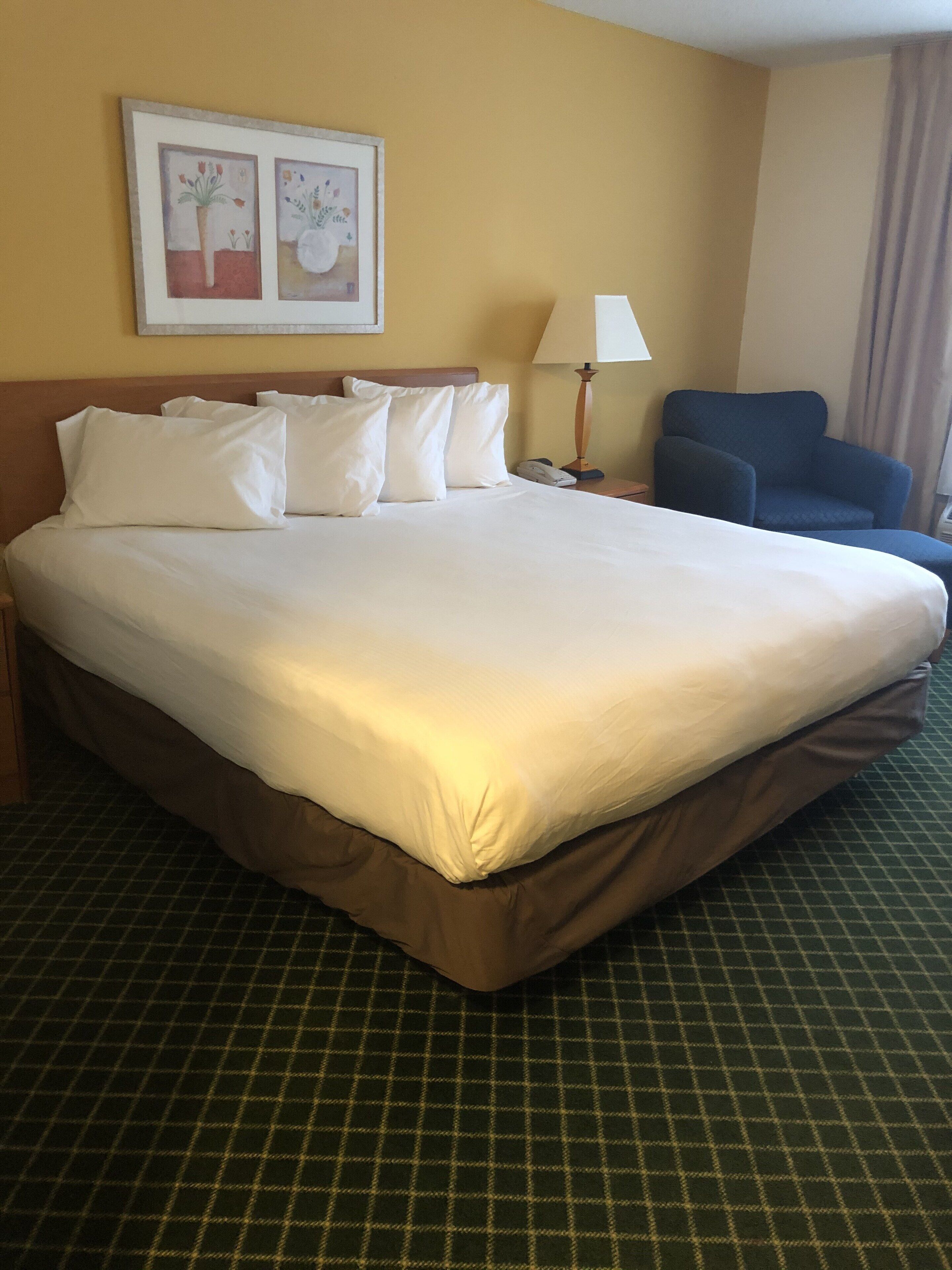 A hotel room with a large bed, a chair, a lamp, and a framed picture on the wall.