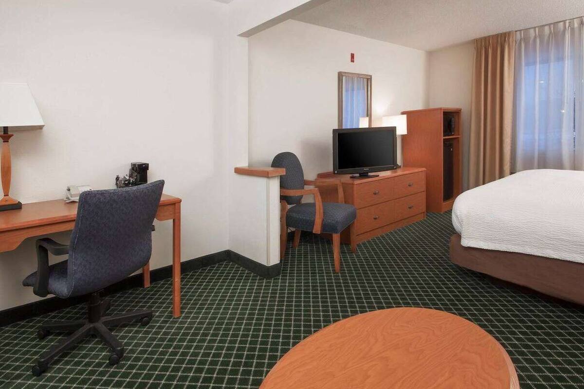 Une chambre d’hôtel comprenant un lit, un bureau avec un ordinateur, une télévision, une chaise, une petite table et une armoire.