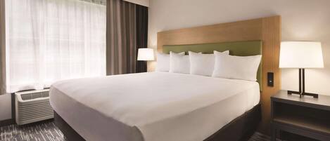 Habitación de hotel con una cama grande, dos lámparas de noche, una ventana con cortinas translúcidas y un aire acondicionado de pared.