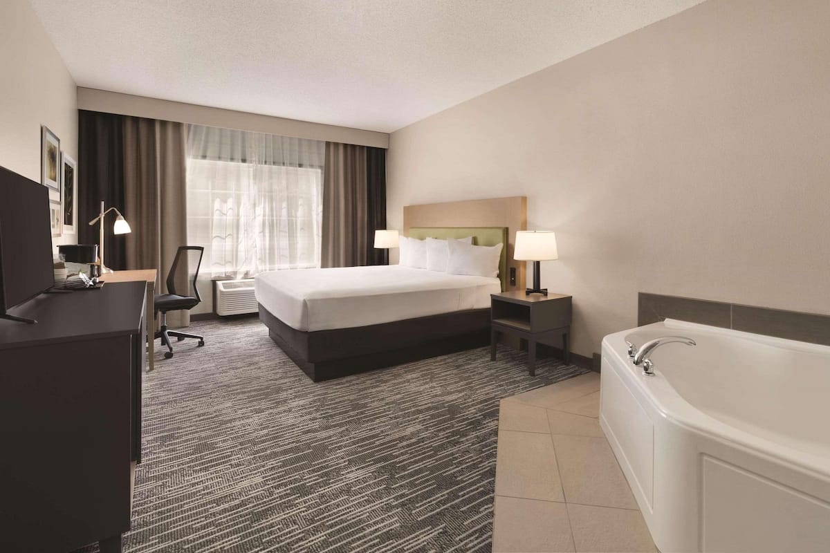 A hotel room with a bed, desk, chair, lamp, and a bathtub.