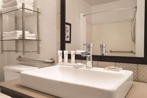 A modern bathroom with a large white sink, a glass towel rack, a toilet, and a shower area.