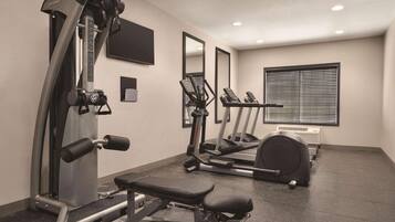 Un gimnasio con máquinas de cardio, equipo de entrenamiento de fuerza y una banca.