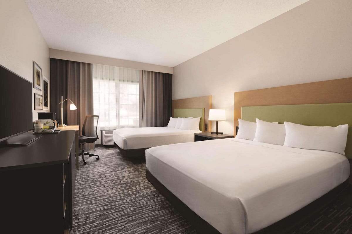 A hotel room with two beds, a desk, a chair, and a window with curtains.