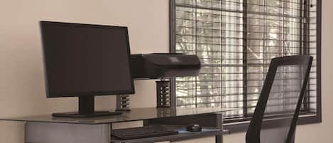 A modern office desk with a computer, keyboard, and mouse, positioned near a window with metal bars.