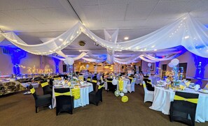 Un salón de banquetes con mesas redondas, manteles blancos y cintas amarillas.