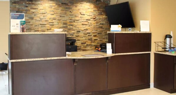 A reception desk with a stone wall backdrop, a flat-screen TV mounted above it, and a coffee machine to the right. - Pocono Inn at Water Gap (Delaware Water Gap)