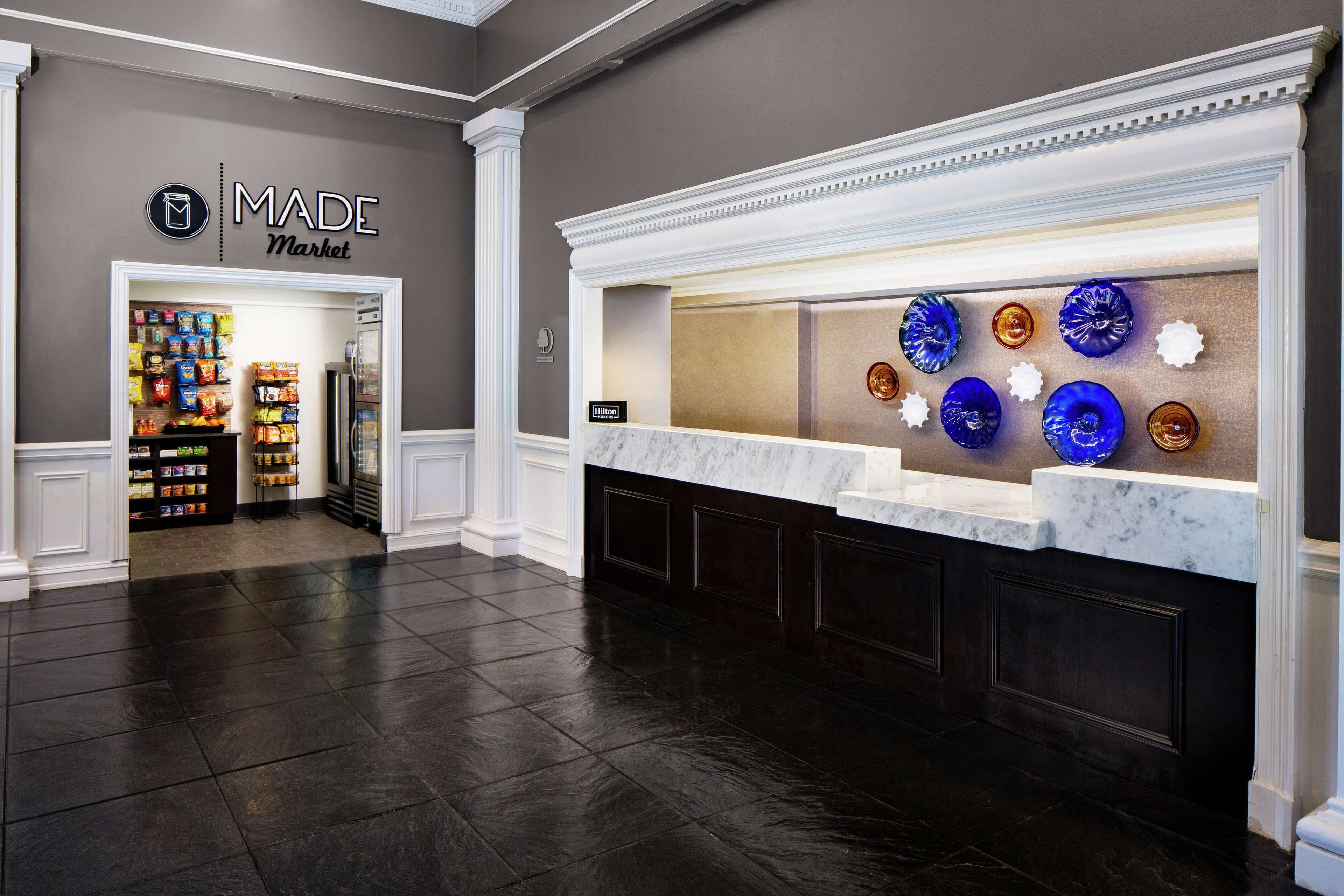 A hotel lobby with a marble reception desk, a display of decorative plates, and a snack area in the background.