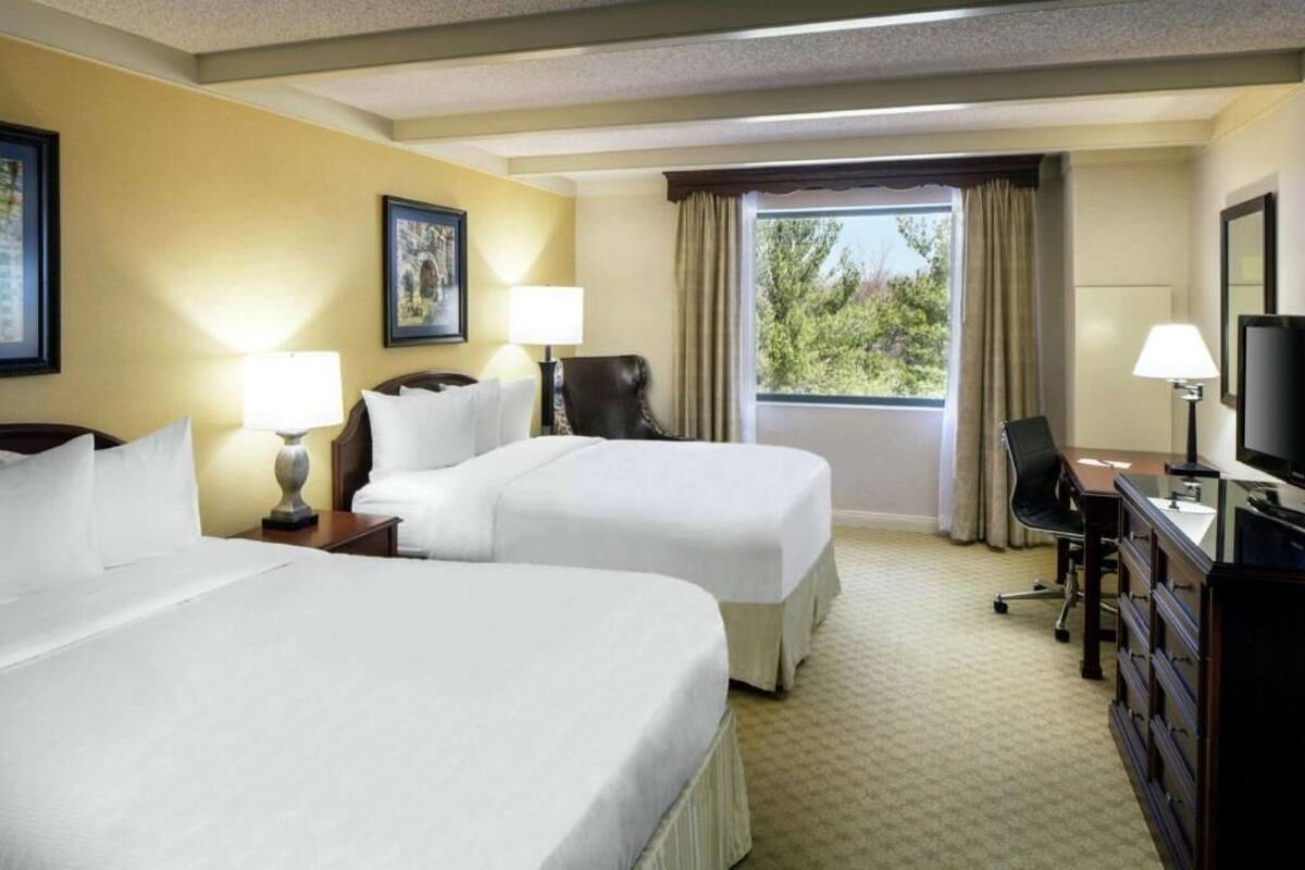 A hotel room with two beds, a desk, a chair, a television, and a window with curtains.