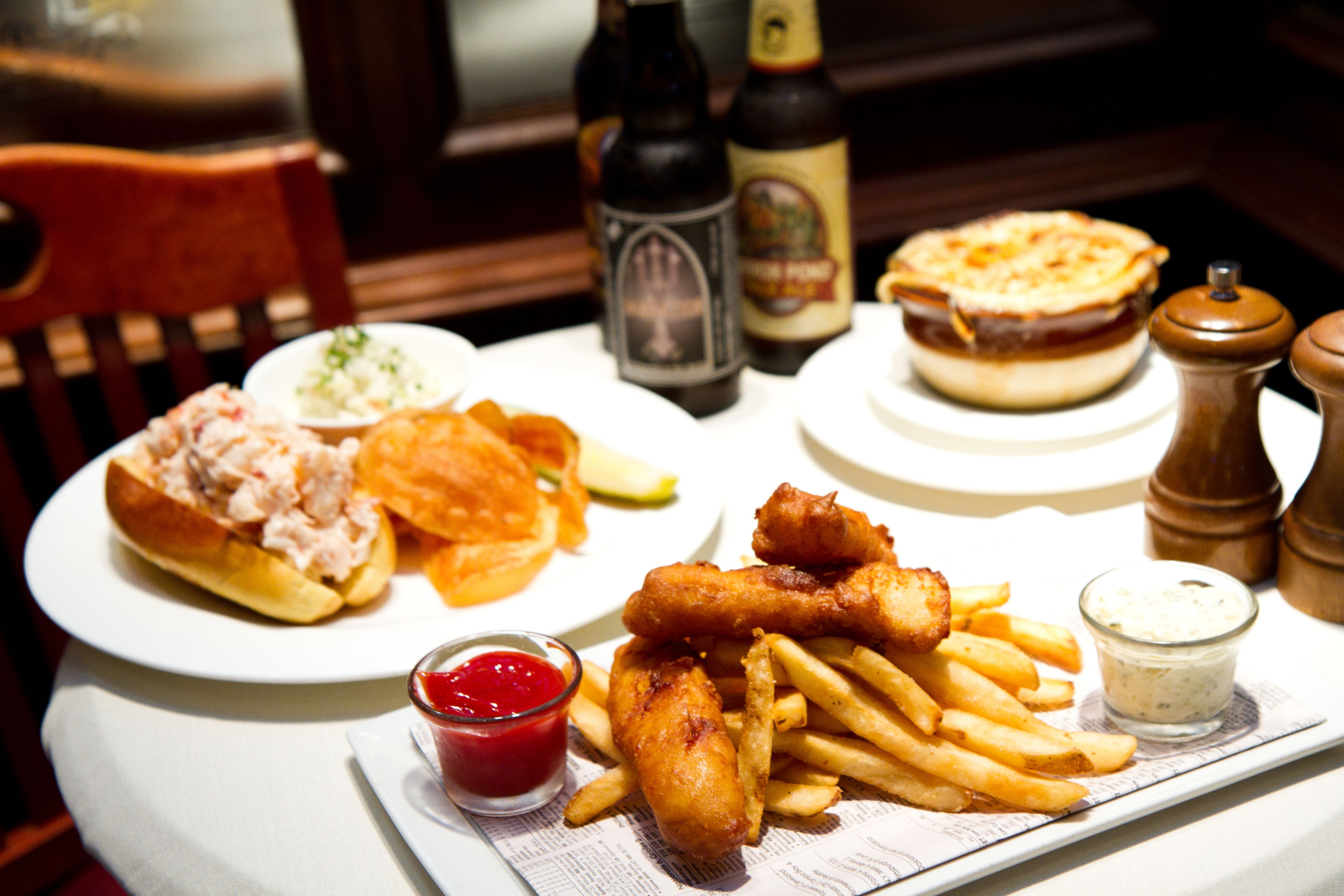 A table with a plate of fish and chips, a sandwich, and a small bowl of ketchup.