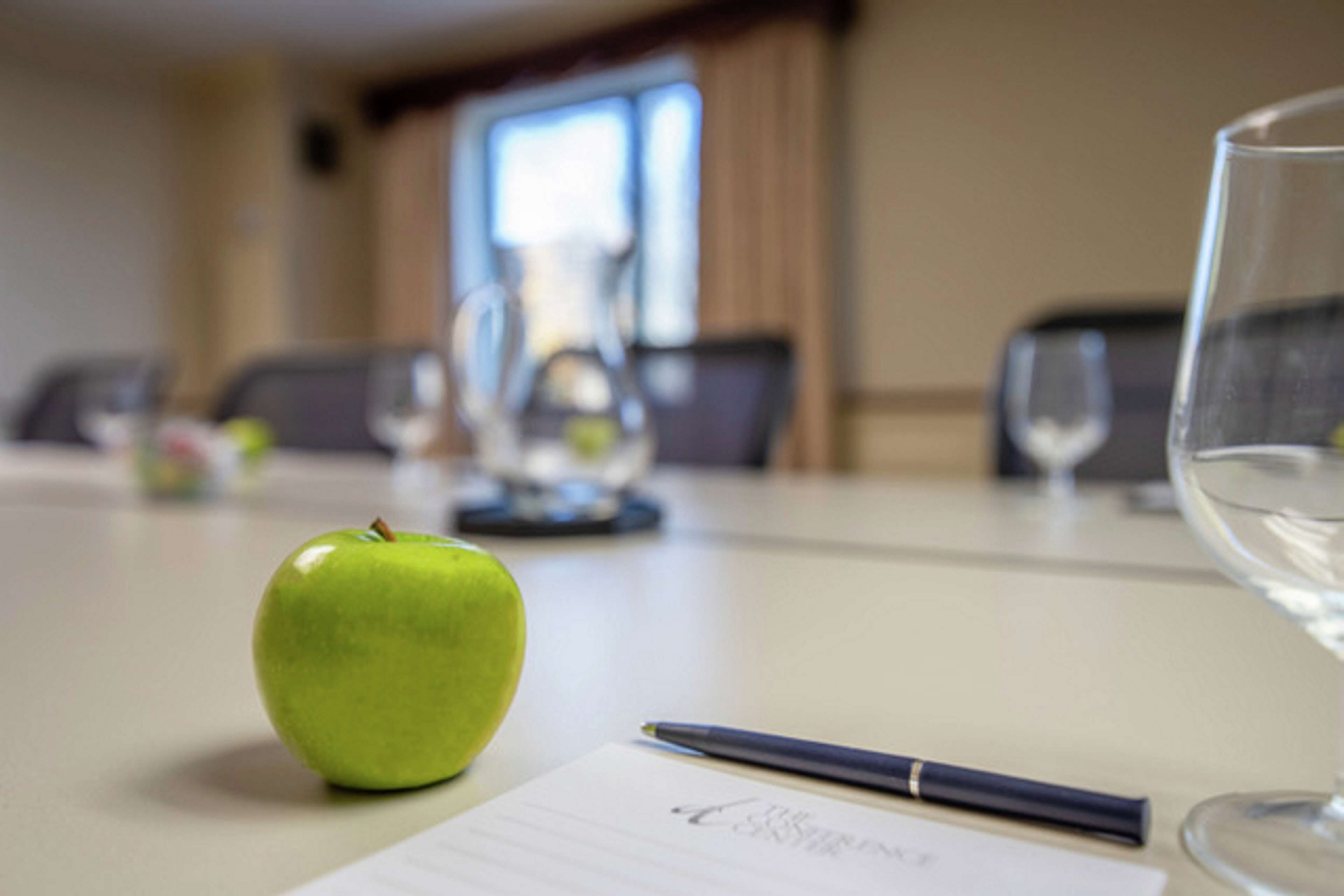 Una mesa de reuniones con una manzana verde, un bolígrafo y un vaso de agua.