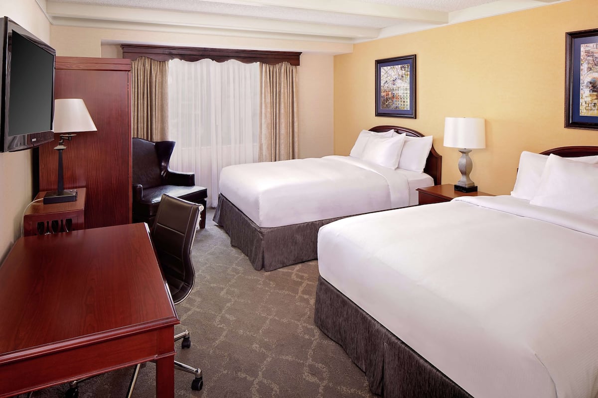 A hotel room with two beds, a desk, a chair, a TV, and a window with curtains.