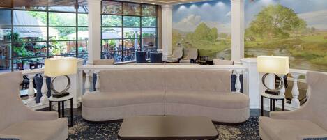 Um hall amplo com um sofá seccional espaçoso, duas poltronas, uma mesa de centro e um mural com paisagem.