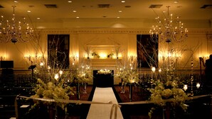 A formal indoor setting with a central aisle, chandeliers, and floral arrangements. - Desmond Hotel Malvern, a DoubleTree by Hilton (Malvern)