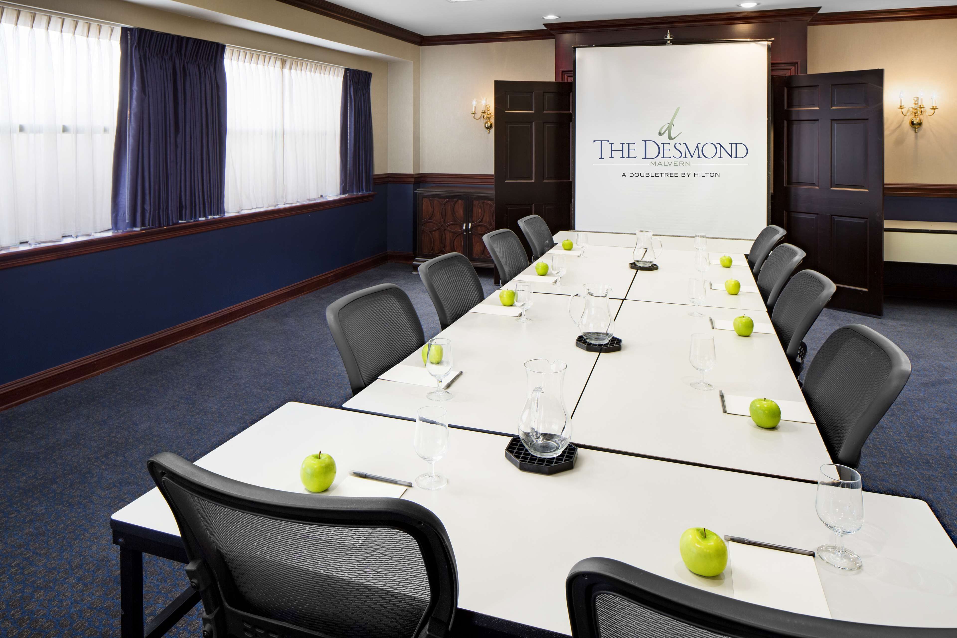 Un salón de conferencias con una mesa larga, sillas y una pantalla para presentaciones.