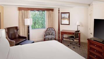 A hotel room with a large bed, a desk, a chair, a TV, and a window with curtains.