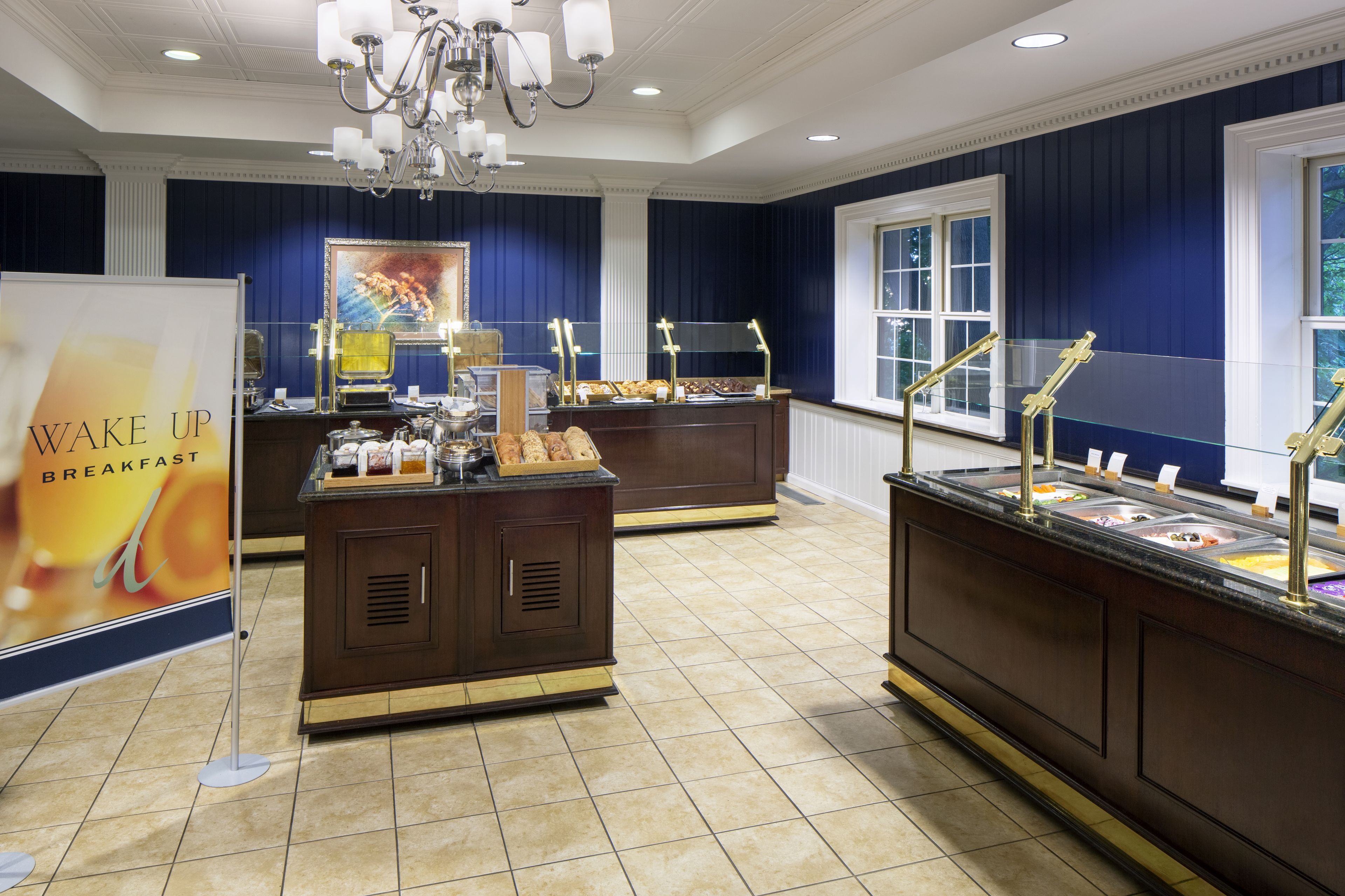 A buffet area with multiple food stations, a sign for breakfast, and a chandelier.
