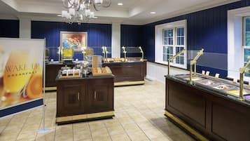 A buffet area with multiple food stations, a sign for breakfast, and a chandelier.