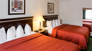 A hotel room with two beds, a nightstand with a lamp, and artwork on the walls.