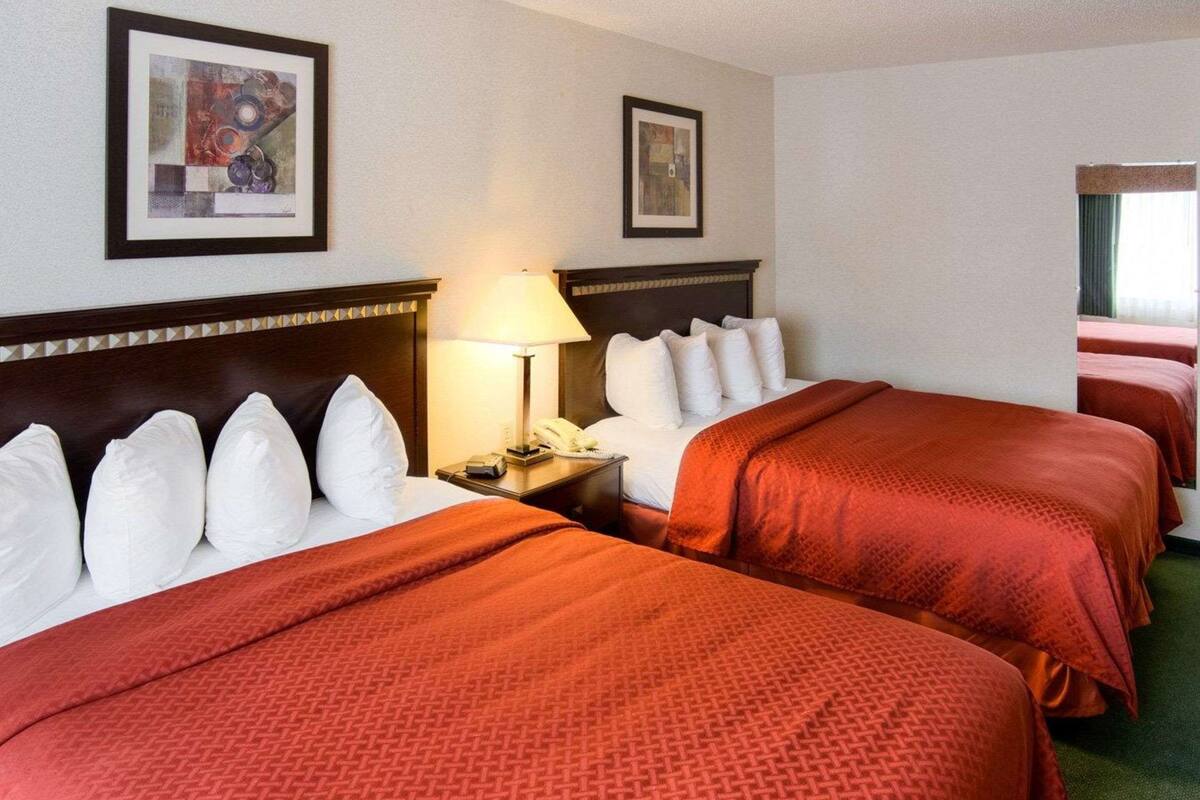 A hotel room with two beds, a nightstand with a lamp, and artwork on the walls.