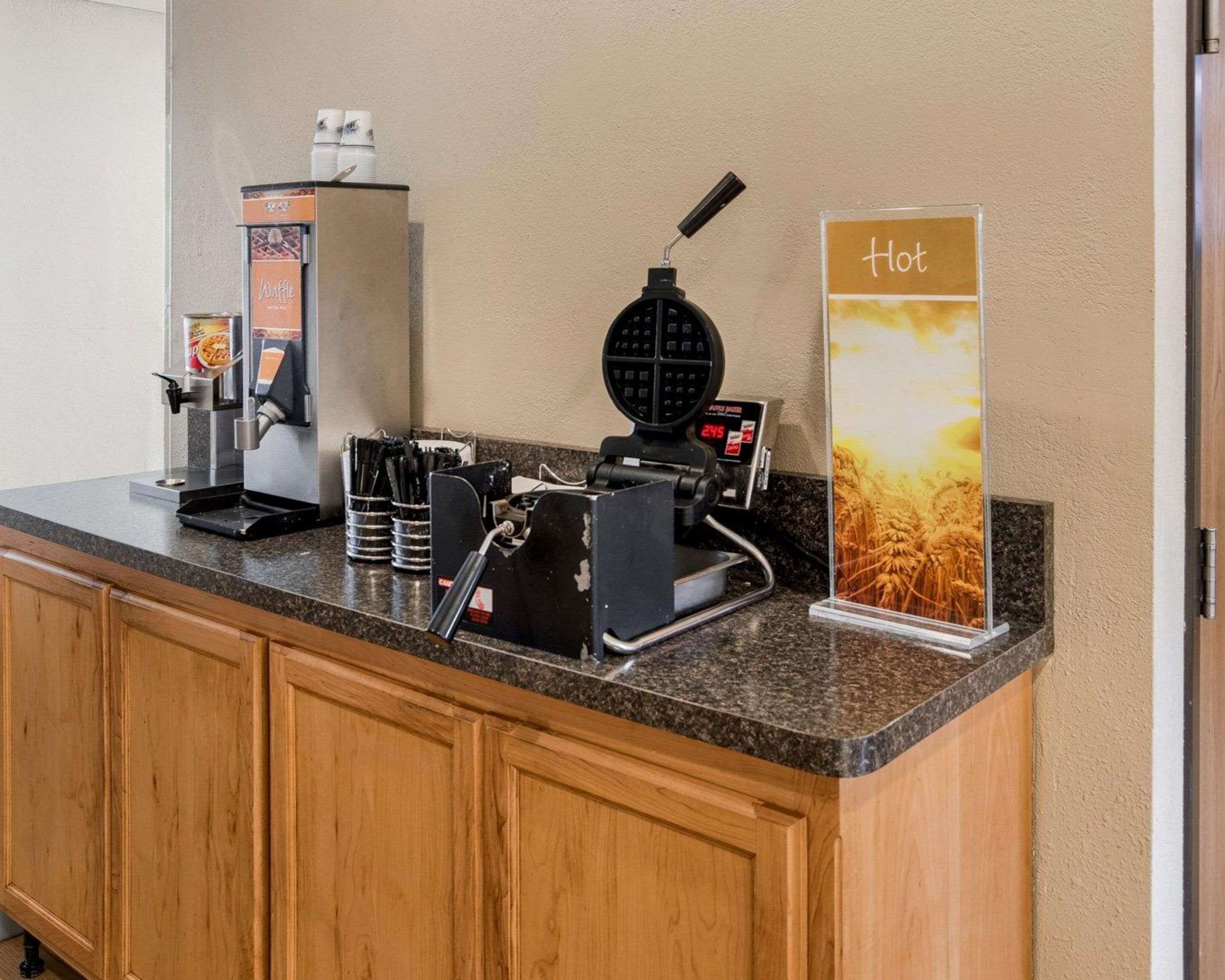 A coffee station with a waffle maker, a coffee machine, and a sign indicating hot beverages.