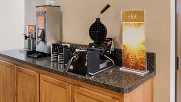 A coffee station with a waffle maker, a coffee machine, and a sign indicating hot beverages.