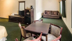 A hotel room with a dining table, four chairs, a sofa, a television, and a minibar.