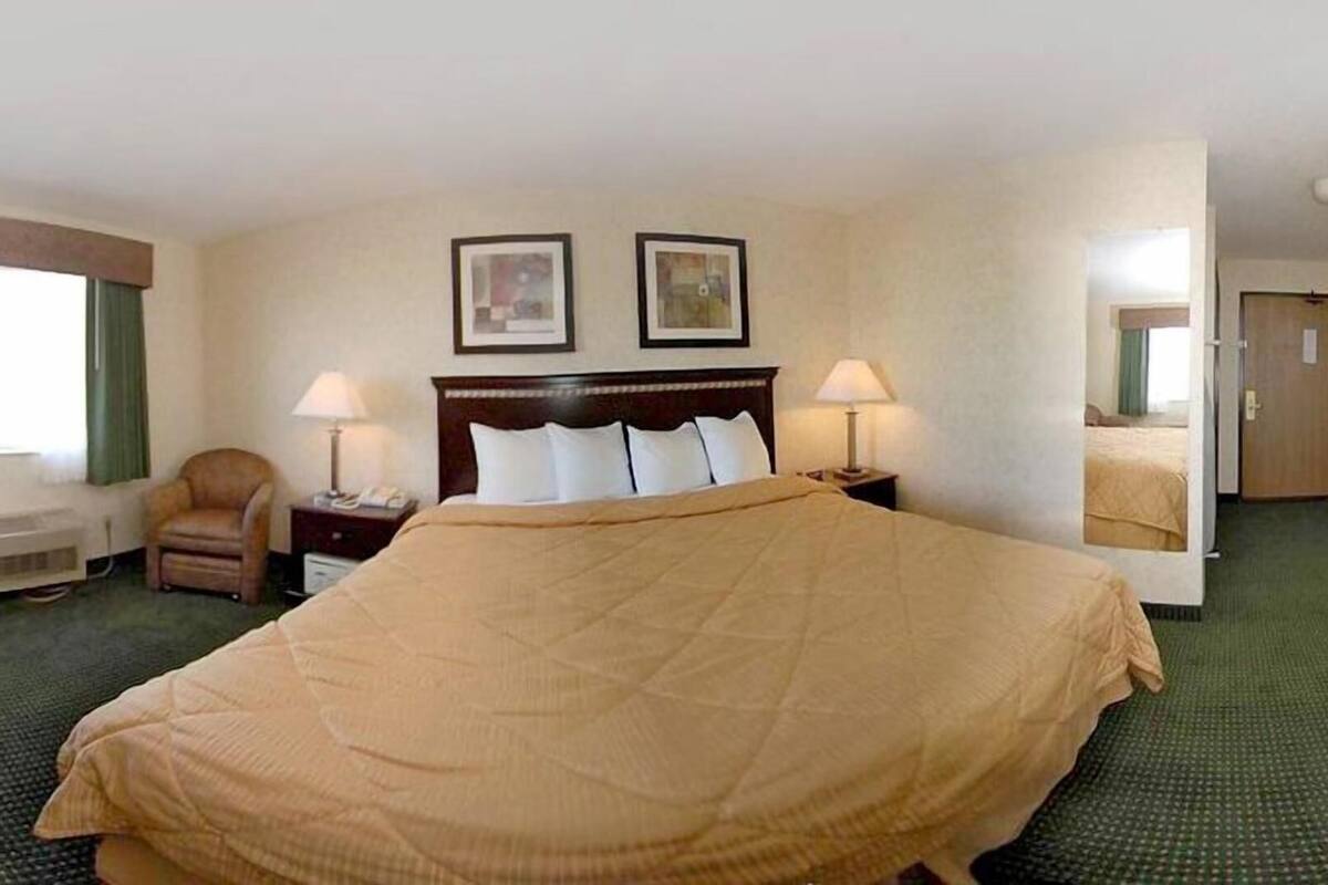 A hotel room with a large bed, two bedside tables with lamps, a chair, a desk, and a window with curtains.
