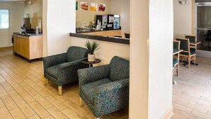 A hotel lobby with patterned armchairs, a reception desk, and a coffee machine.
