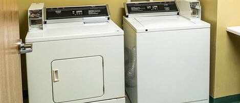 Two stacked front-loading washers in a laundry room with a wooden door and a green bench.