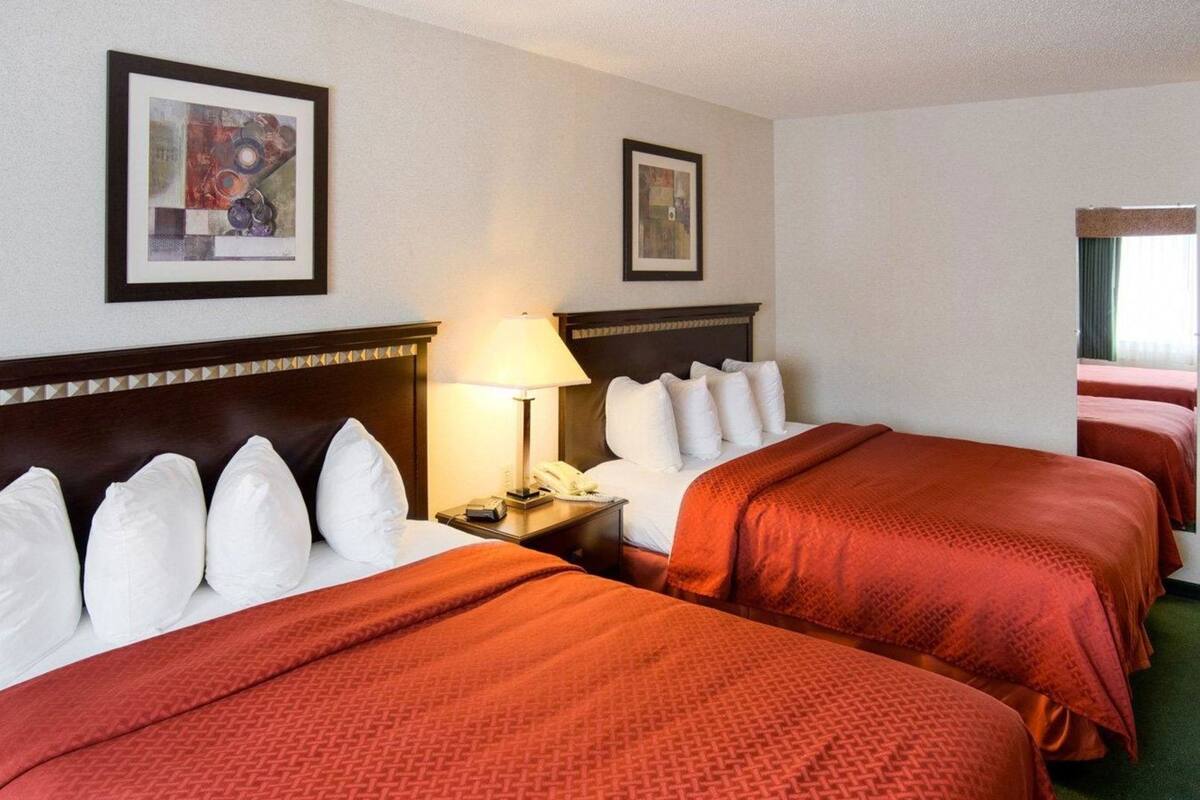 A hotel room with two beds, a nightstand with a lamp, and two framed artworks on the walls.