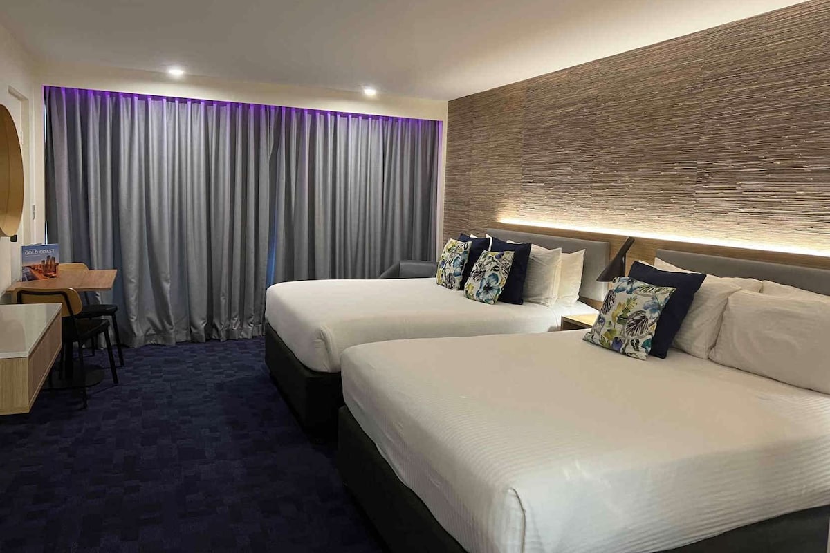 A hotel room with two beds, a desk, and a large window with curtains.