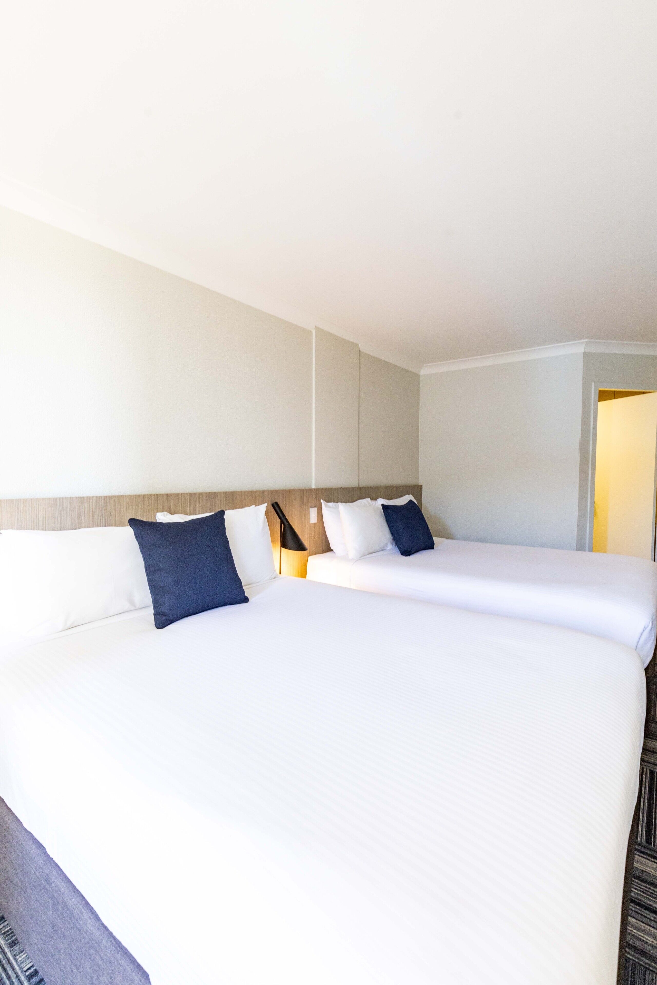 A hotel room with two beds, a wooden headboard, and a nightstand with a lamp.