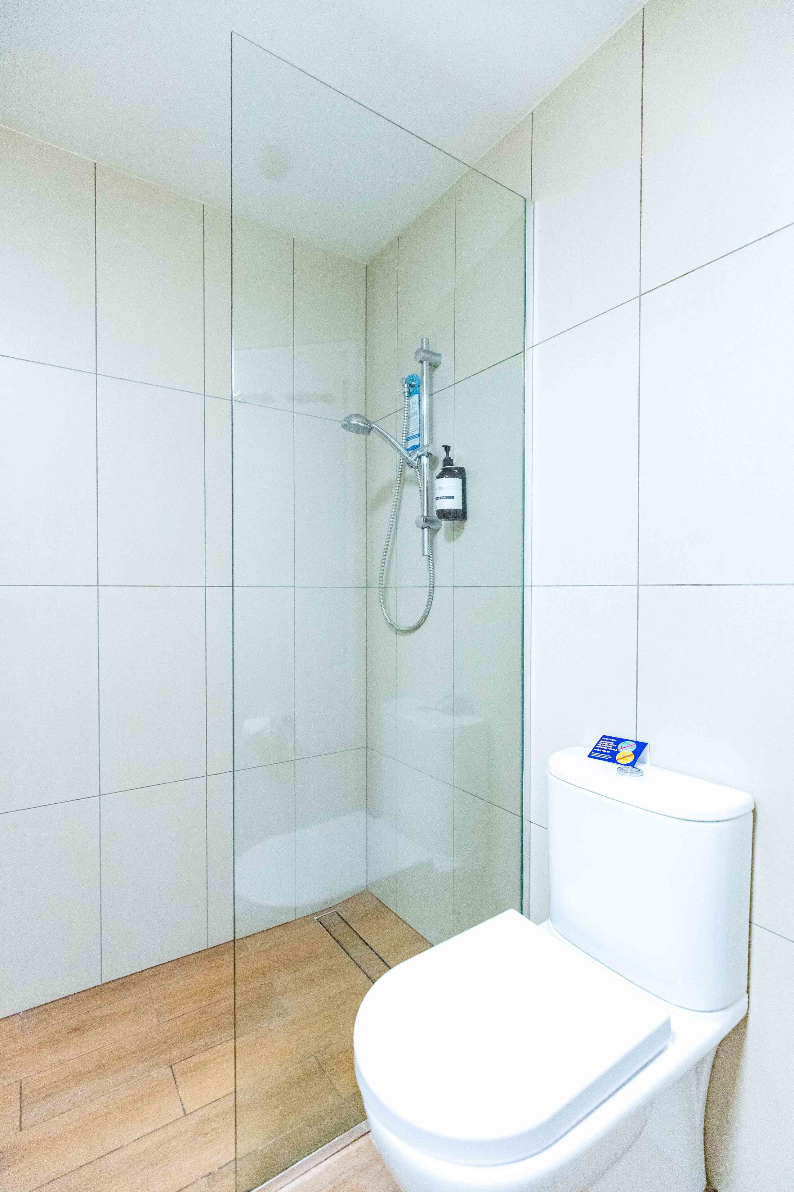Ein Badezimmer mit Duschkabine aus Glas, einer weißen Toilette und einem gefliesten Boden.