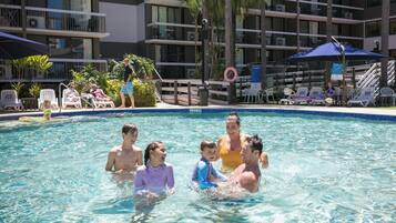 Ein Poolbereich mit Liegestühlen und Sonnenschirmen, umgeben von einem mehrstöckigen Gebäude mit Balkonen.