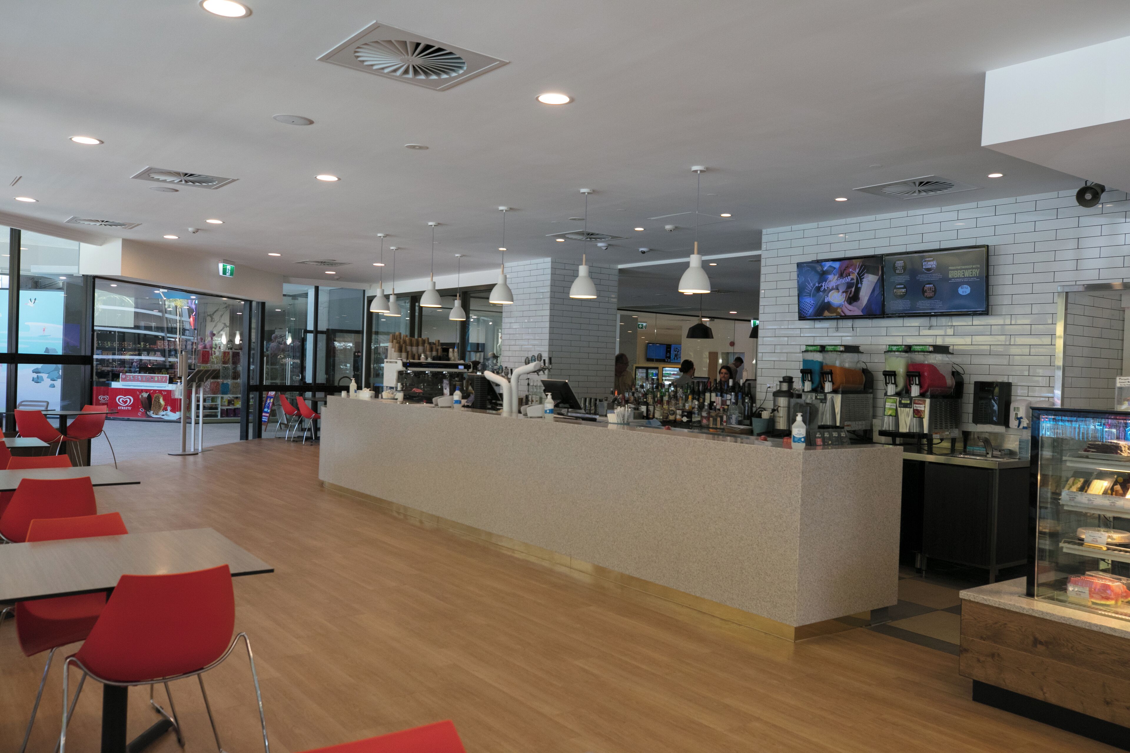 Een modern café met een balie, een zithoek en een televisiescherm dat iets toont.