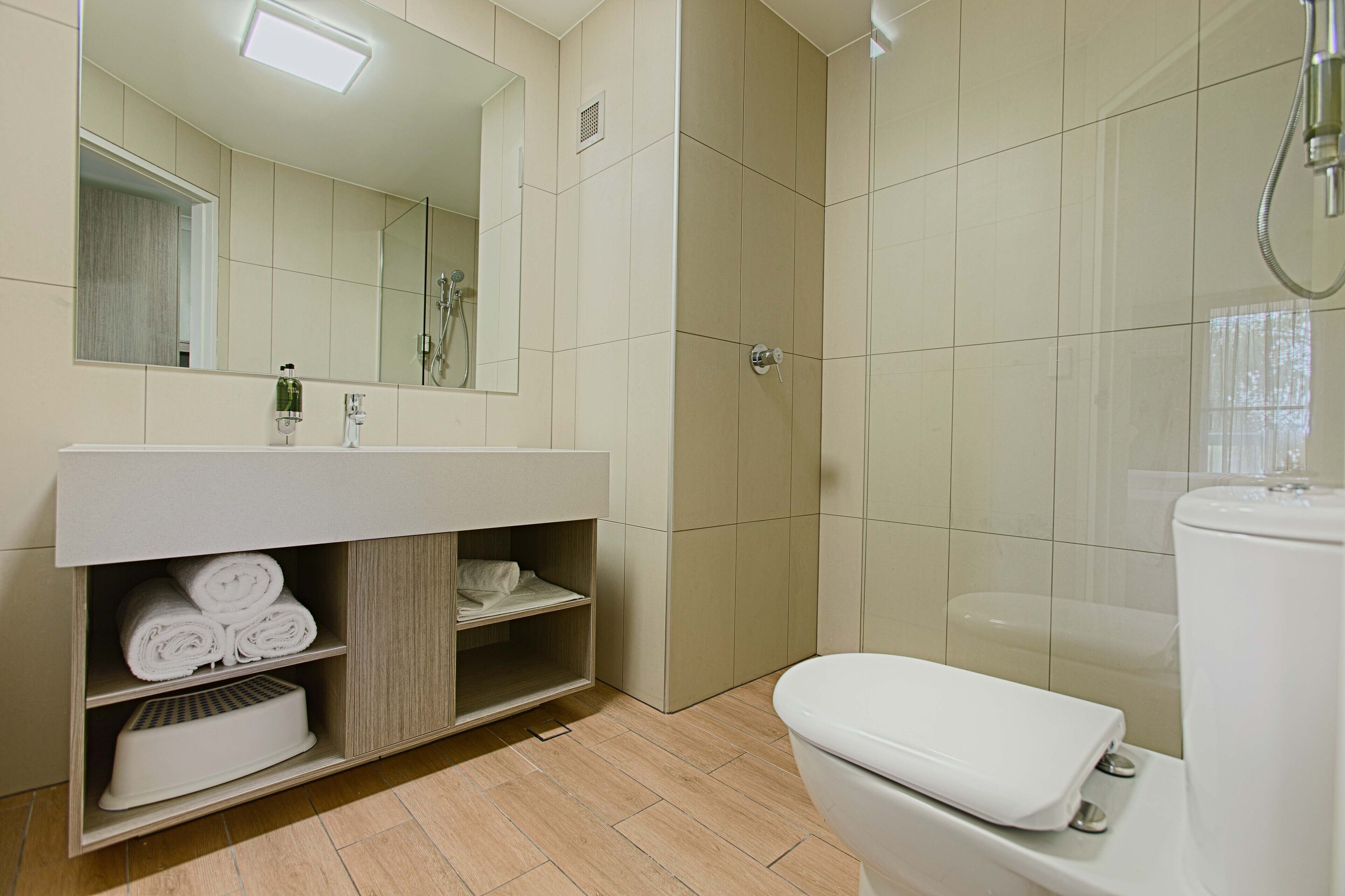 Une salle de bain moderne avec un lavabo blanc, un miroir et des toilettes. On y trouve un espace douche avec une porte en verre et un porte-serviettes avec des serviettes pliées.