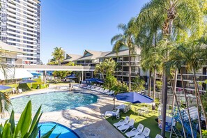 Área de piscina de hotel com espreguiçadeiras, guarda-sóis e palmeiras.