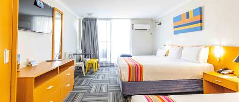 Una habitación de hotel con cama, escritorio, silla, televisor y ventana con cortinas.