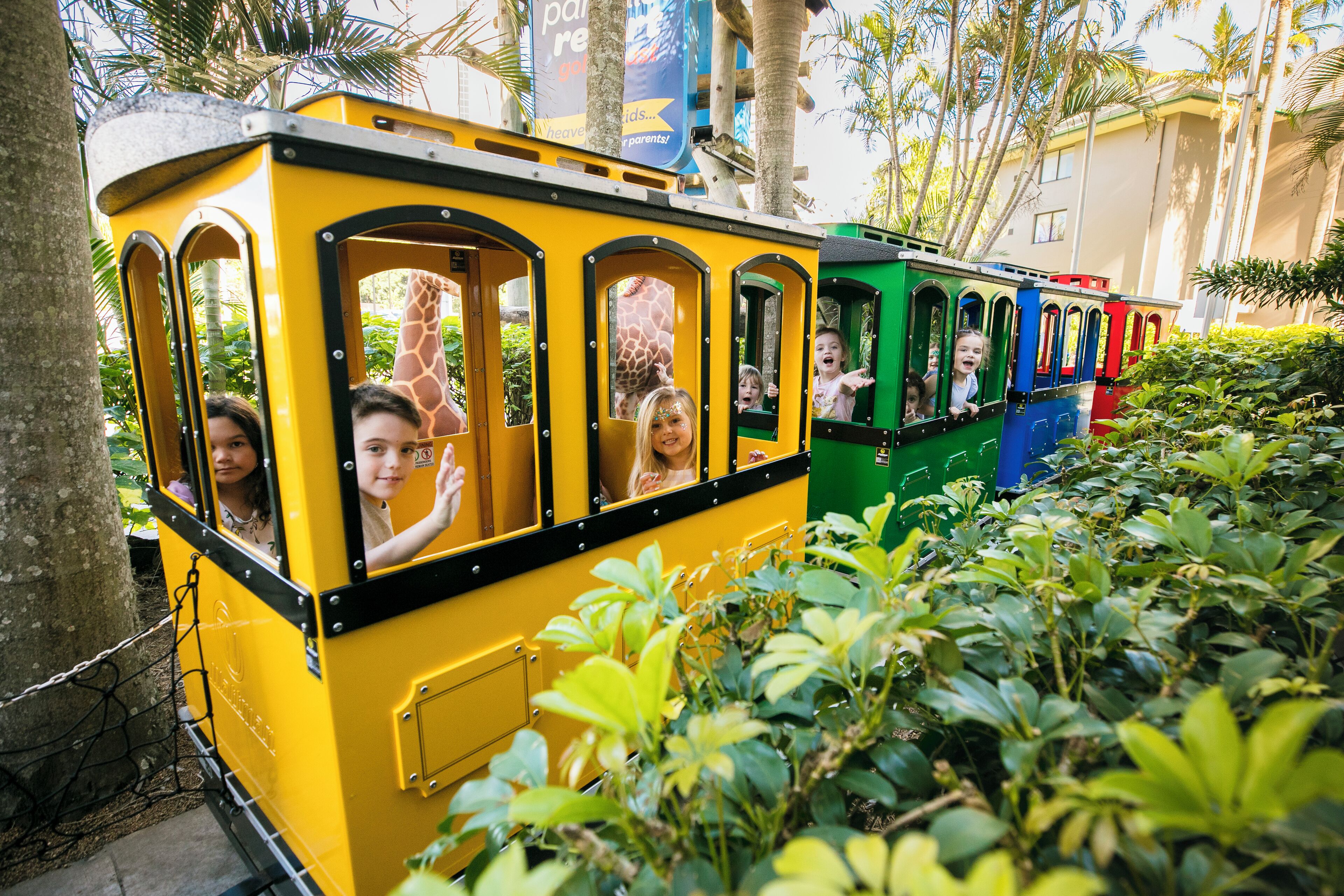 Een gele en groene trein met passagiers, omringd door weelderige begroeiing.