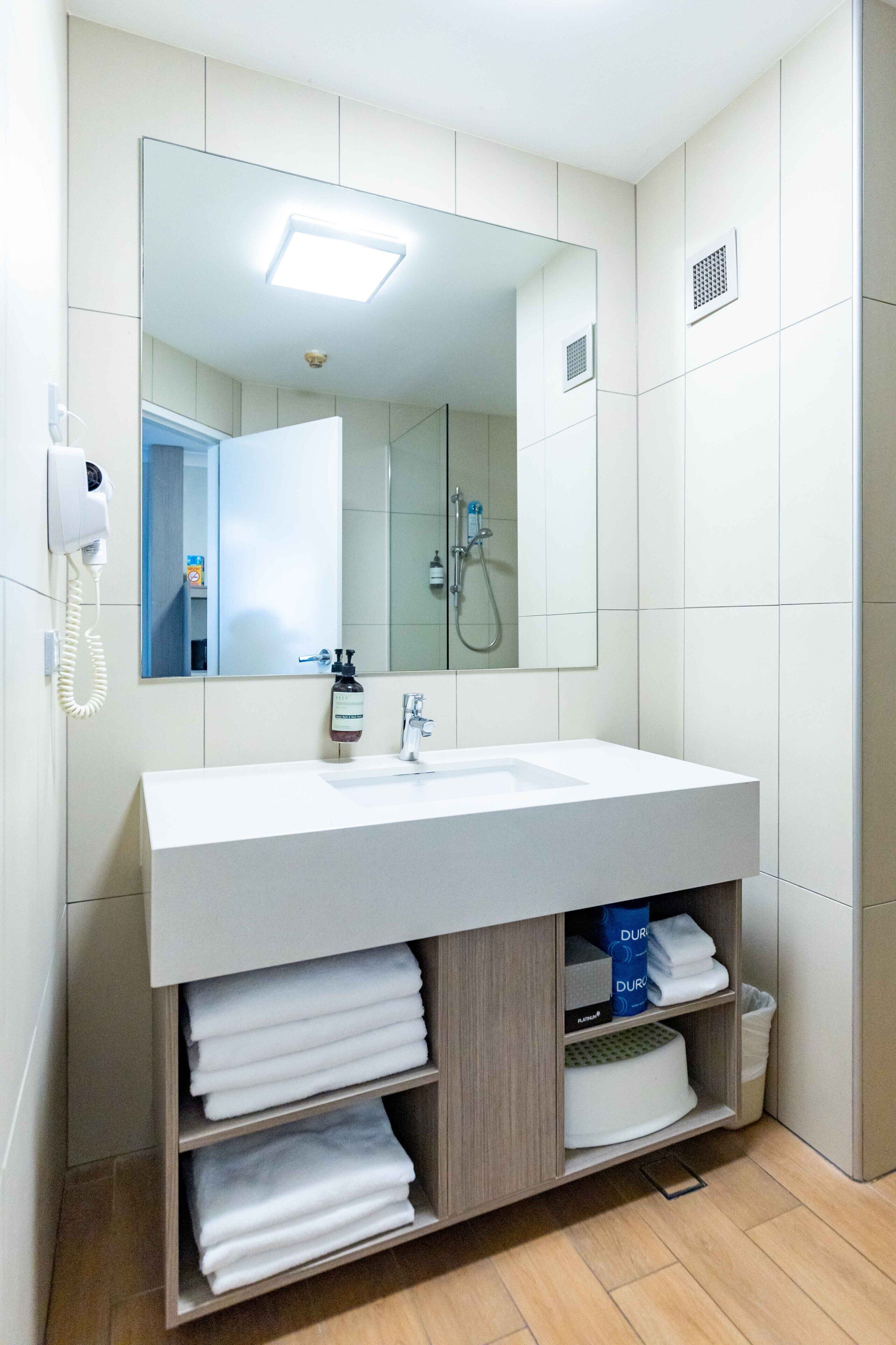 A modern bathroom with a large mirror, white sink, and built-in towel storage.