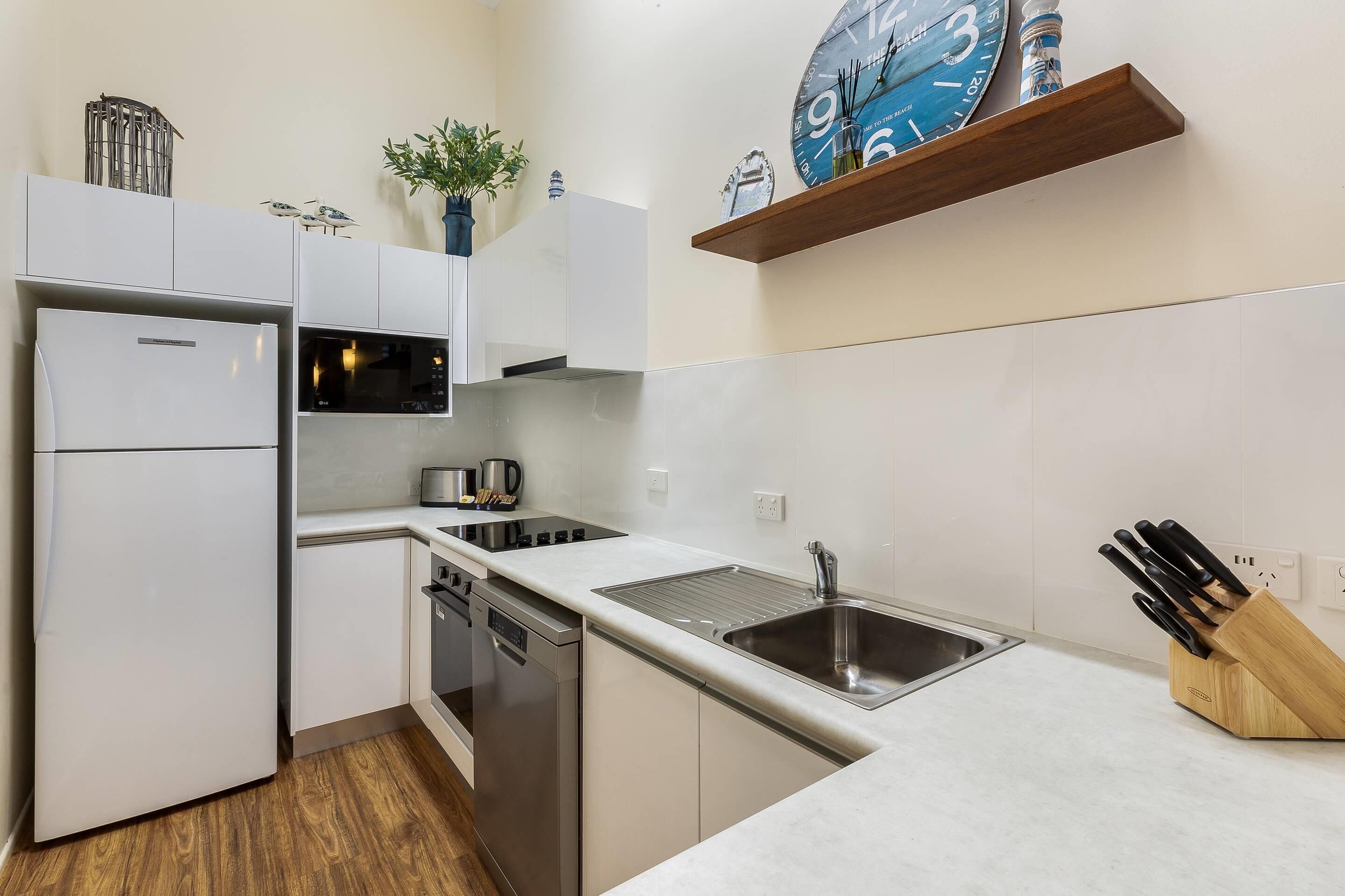 Een moderne keuken met witte kastjes, roestvrijstalen apparatuur, een spoelbak en een messenblok.